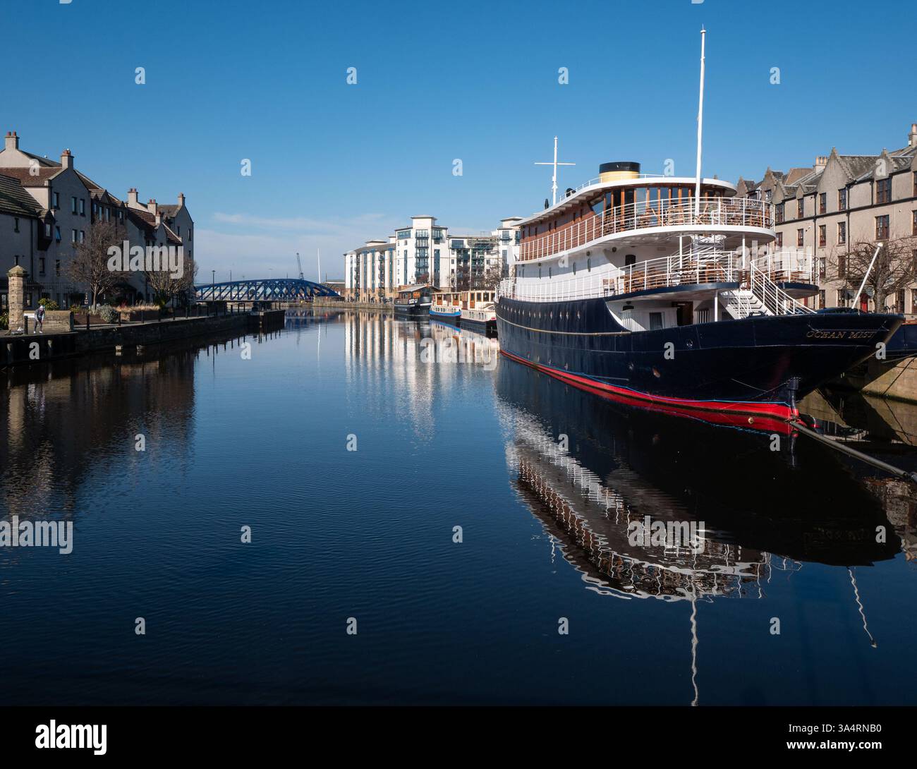 Leith, Édimbourg, Écosse, Royaume-Uni, 19 mars 2025. Météo britannique : le deuxième jour de soleil glorieux et un ciel bleu clair mais encore froid. Sur la photo : hôtel flottant Ocean Mist et péniches sur le rivage se reflètent dans l'eau de la rivière Leith. Crédit : Sally Anderson/Alamy Live News Banque D'Images