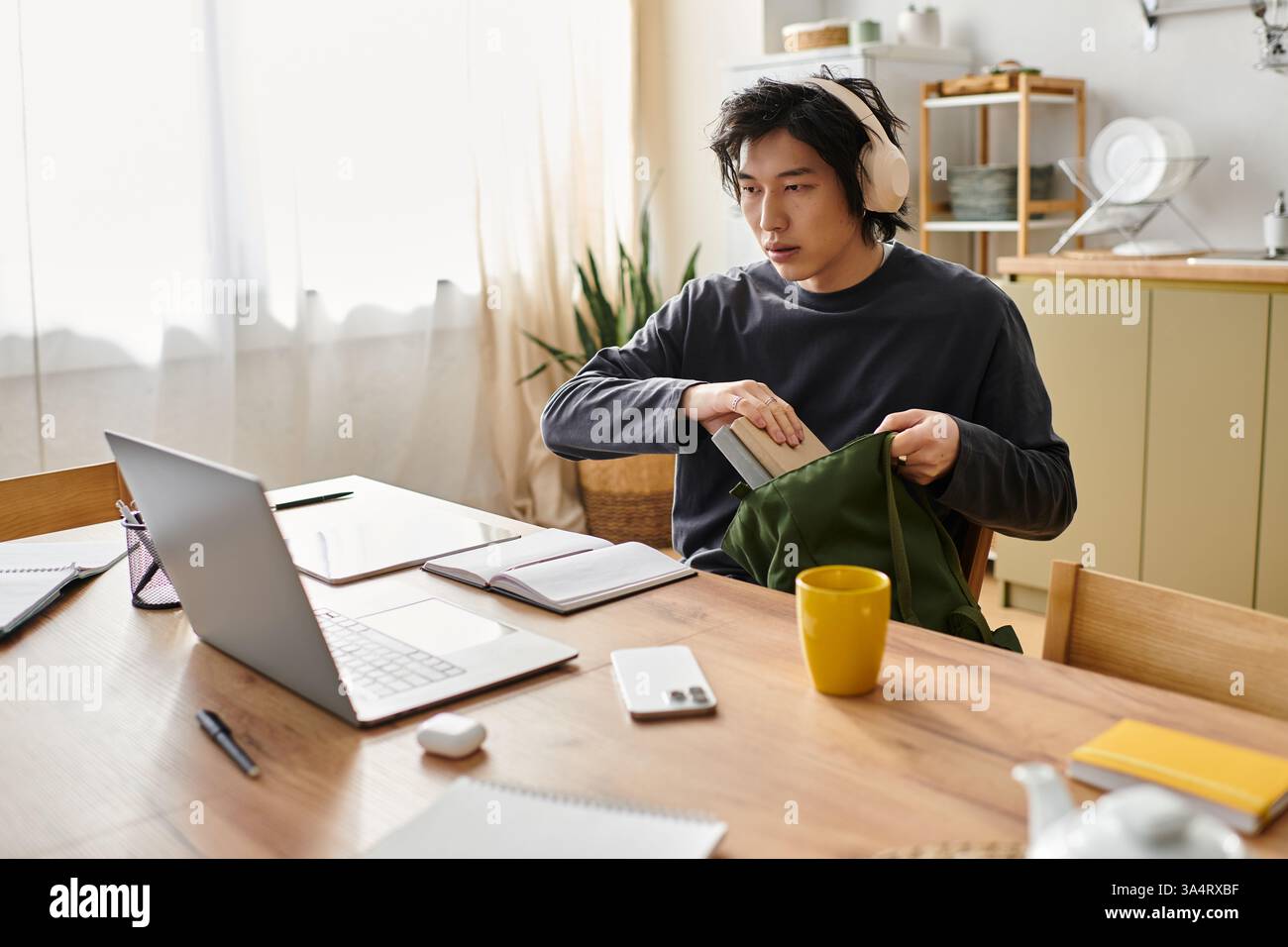 Un jeune homme se concentre sur son cours en ligne tout en préparant son matériel à la maison. Banque D'Images