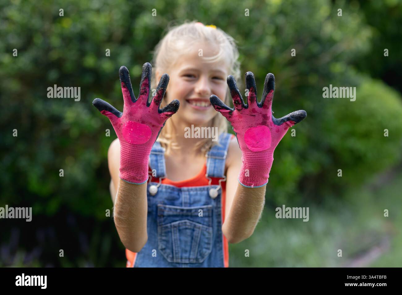 Fille souriante dans le jardin montrant les mains sales dans des gants roses, profiter du plaisir en plein air, copier l'espace Banque D'Images