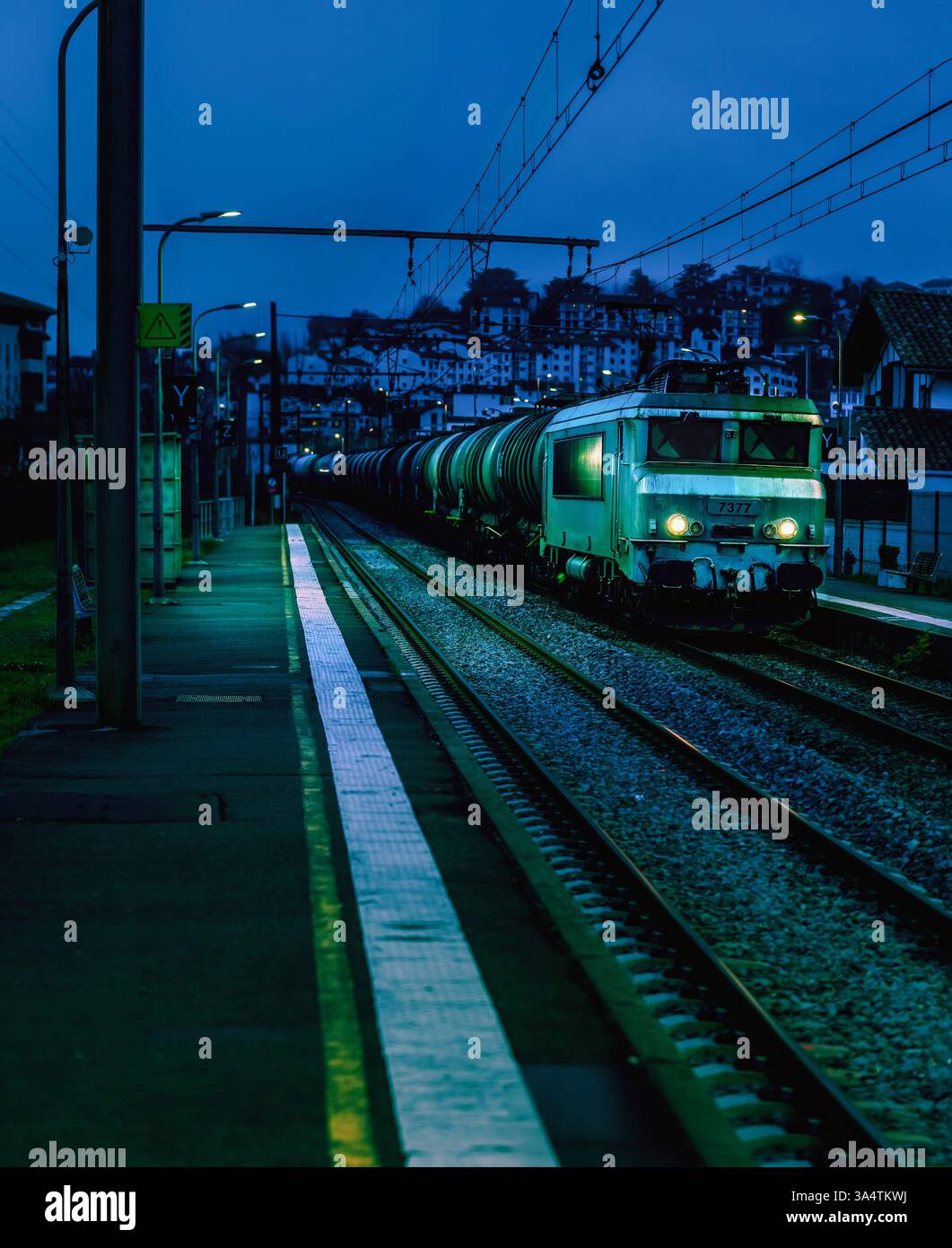 Un train de marchandises passant par un quai de gare tranquille à la tombée de la nuit. Banque D'Images