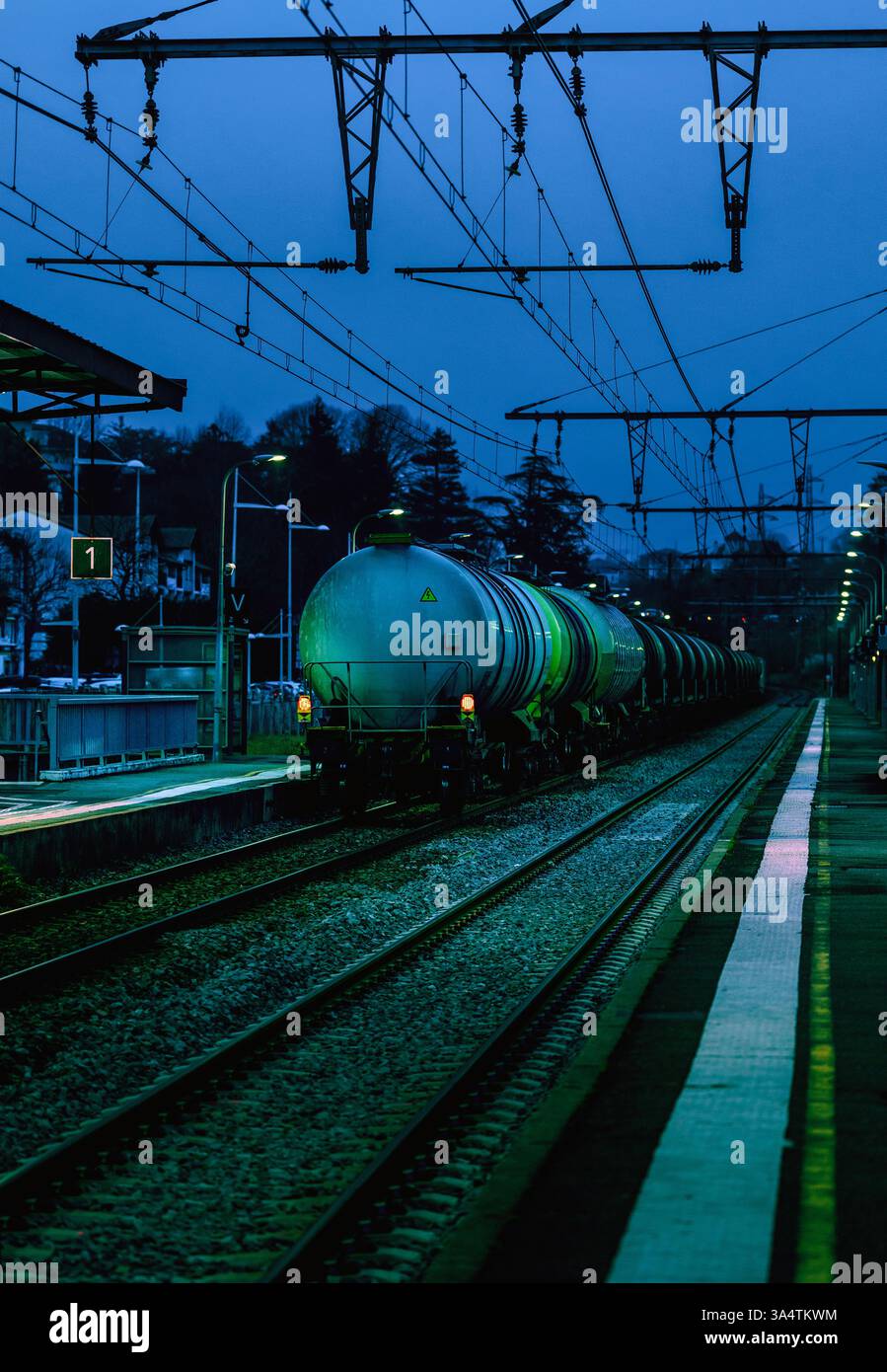 Le camion-citerne de queue d'un train passe par un quai de gare tranquille à la tombée de la nuit. Banque D'Images