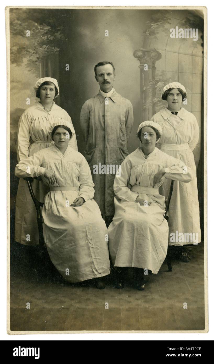 Original WW1 Era studio portrait carte postale des ouvrières de munitions féminines avec contremaître, portant des capuchons élastiques, généralement portés pour garder les cheveux hors de la machinerie. Salopettes en lin blanc, emplacement inconnu, circa 1916, Royaume-Uni Banque D'Images