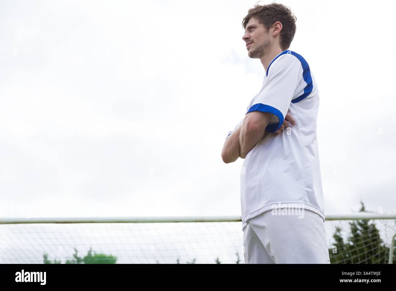 Joueur de football debout en toute confiance sur le terrain, portant un uniforme blanc et bleu, espace de copie Banque D'Images