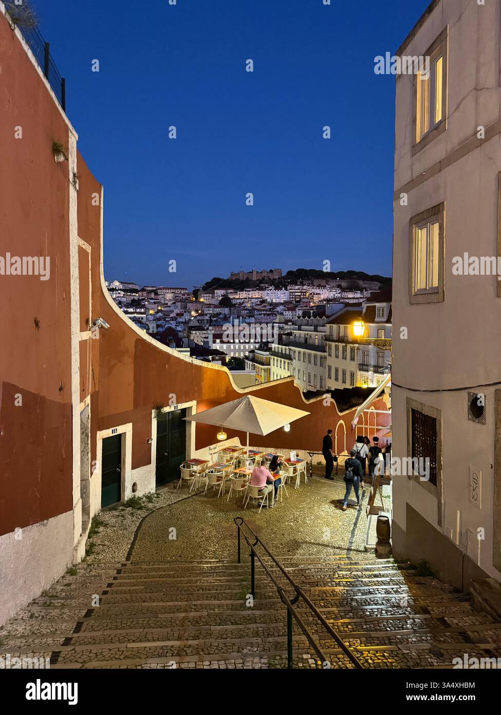 Une vue en soirée sur Lisbonne, en descendant les marches de Rua do Duque vers le Castelo do São Jorge avec un restaurant en plein air au premier plan. - Image de stock capturée avec un smartphone