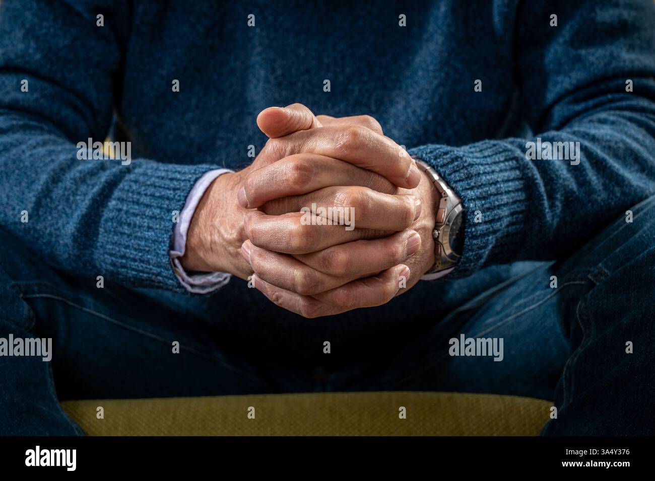 Gros plan des mains serrées d’un homme âgé, symbolisant la contemplation, le stress ou la pensée profonde, avec un accent sur les détails et les émotions. Banque D'Images