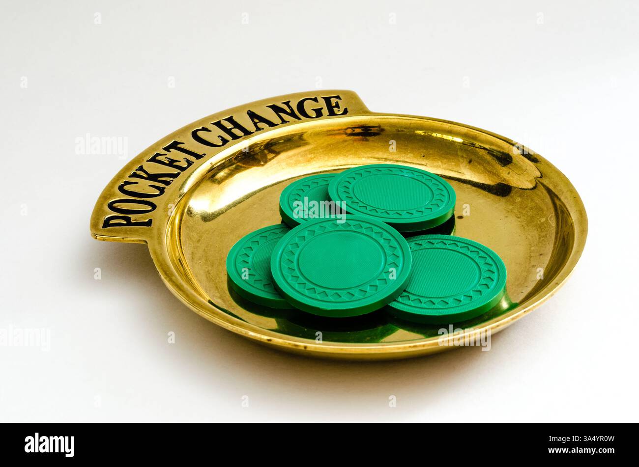 Plateau de changement de poche en laiton avec lettrage noir et une pile circulaire de jetons de poker sur fond blanc. Banque D'Images