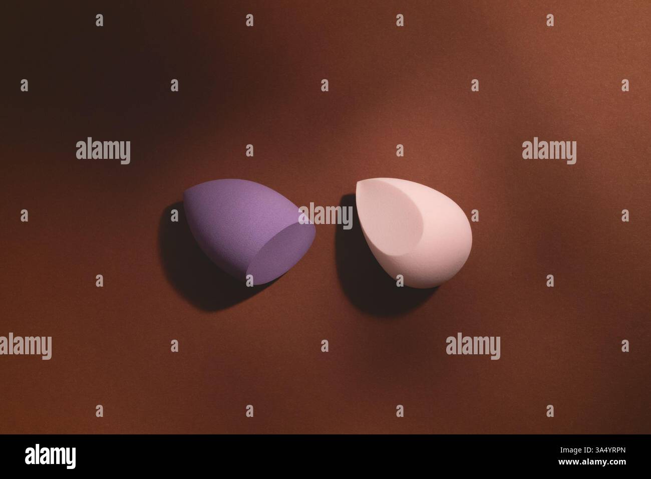 Cosmétiques éponges de maquillage de forme et de couleur différentes sur un fond brun foncé avec des ombres. Composition élégante et artistique avec des outils de beauté. Banque D'Images