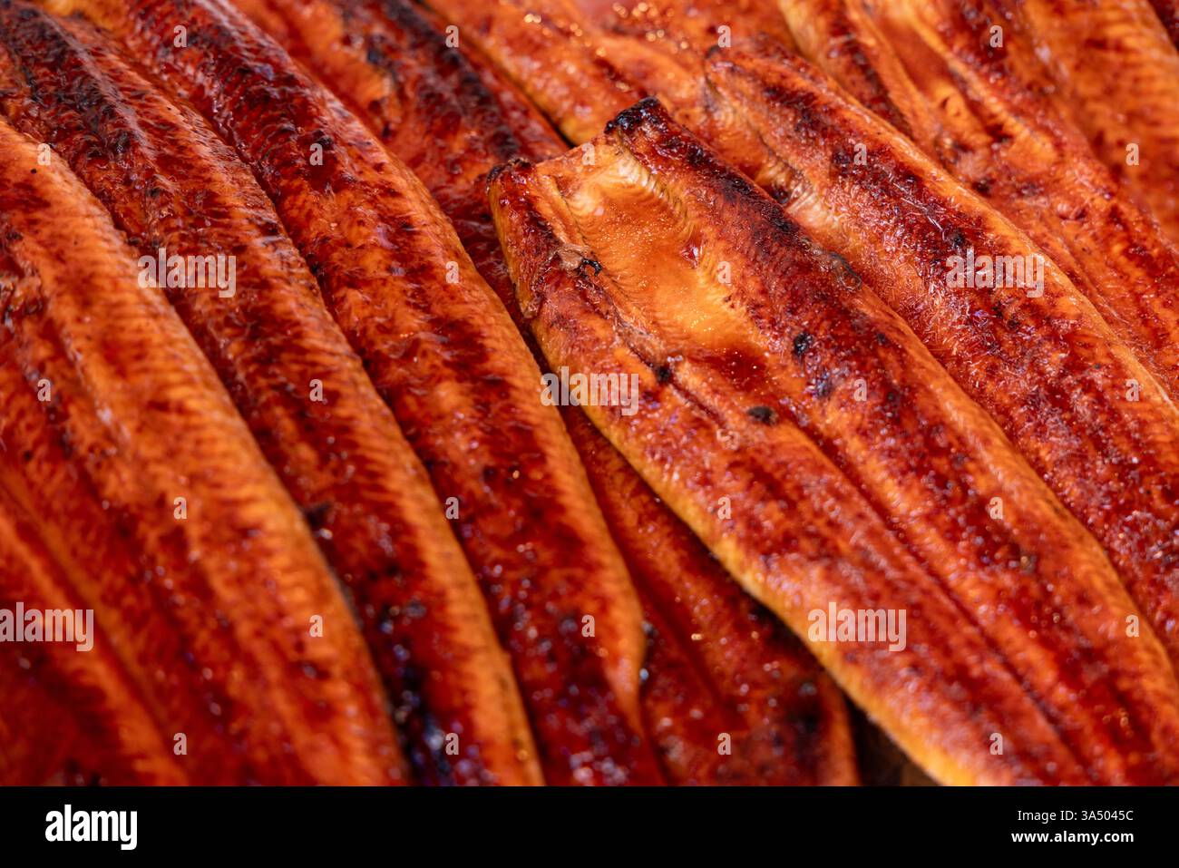 Gros plan de filets d'unagi grillés enrobés d'un glaçage de soja sucré avec une texture légèrement carbonisée mettant en valeur leur riche saveur d'umami sur un marché de fruits de mer i. Banque D'Images