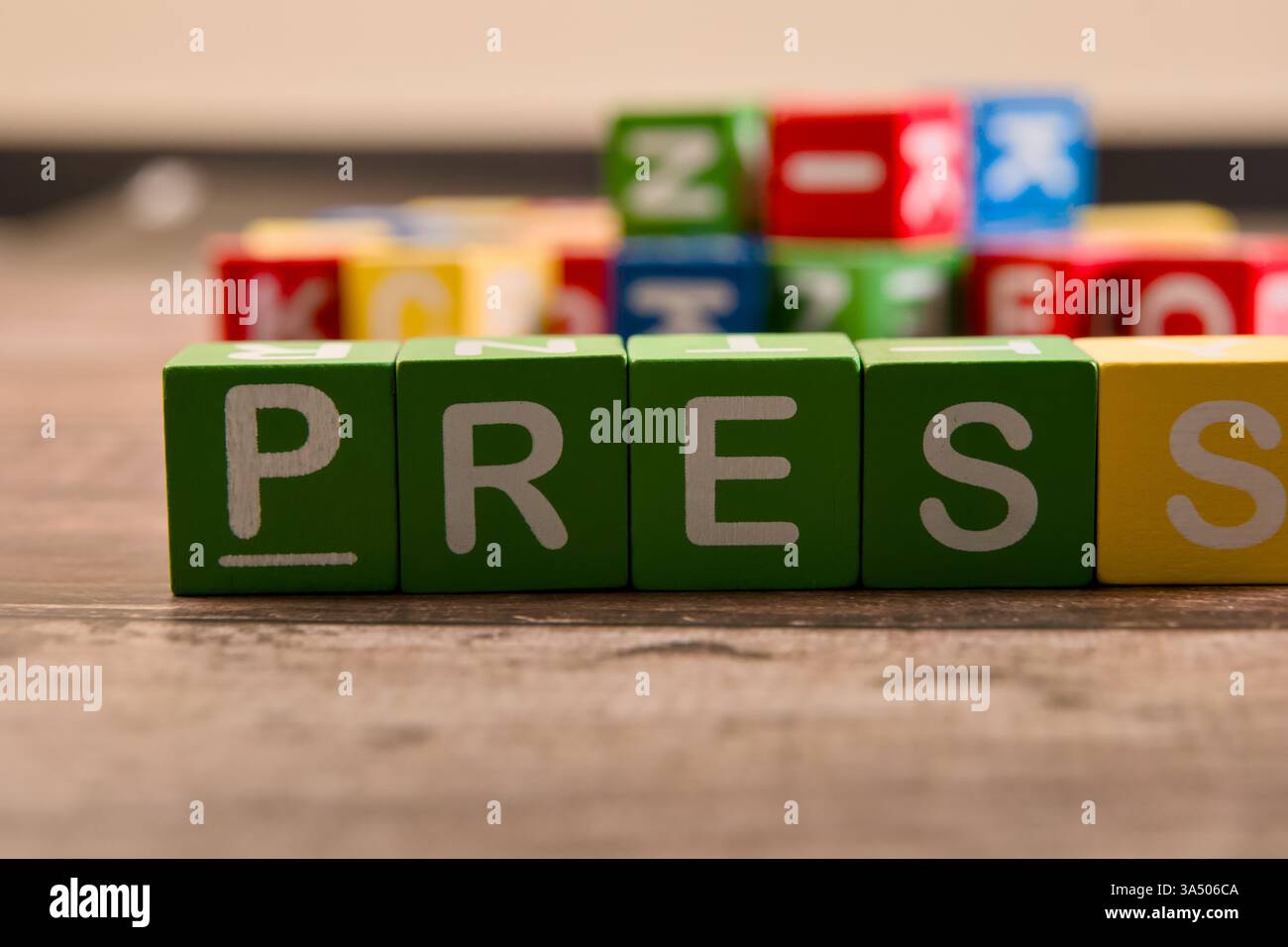 Des blocs colorés sont disposés sur un plancher en bois, affichant en évidence le mot presse parmi diverses autres lettres. Banque D'Images