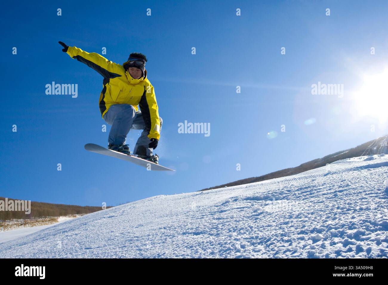 Jeune homme chinois snowboard en plein air un jour d'hiver. Photo d'action dynamique idéale pour les sports d'hiver, le ski et les campagnes de style de vie actif. Le ciel dégagé et le cadre du complexe le rendent idéal pour les voyages et les loisirs en plein air. Banque D'Images