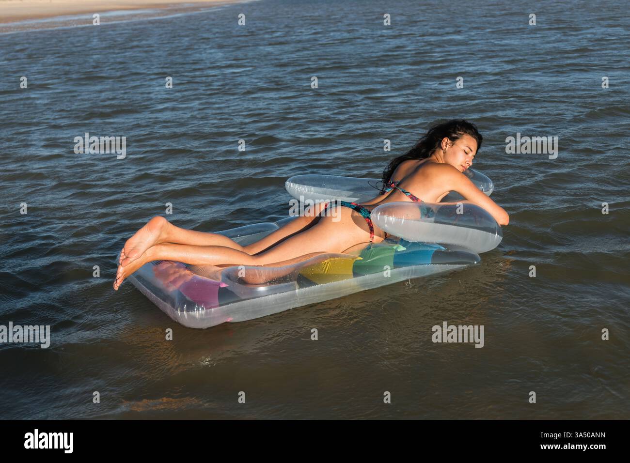Femme Latina avec les yeux fermés se relaxant sur un matelas gonflable flottant dans la mer. Elle profite d'un moment d'été insouciant avec l'eau et la lumière du soleil. Idéal pour les vacances, les voyages et les campagnes de style de vie à la plage. Banque D'Images
