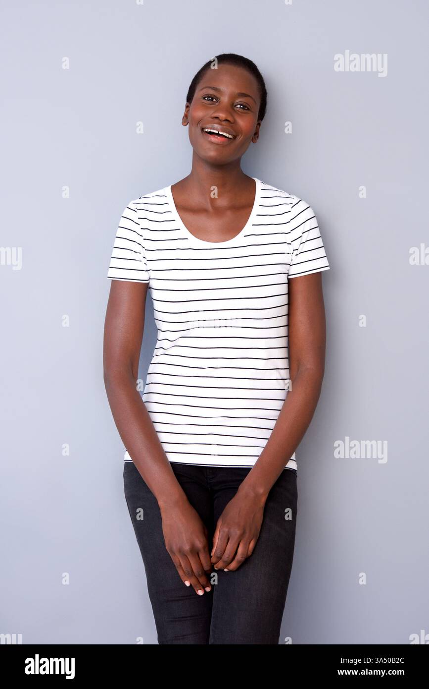 Portrait d'une jeune femme afro-américaine souriante sur fond gris de studio. Ce headshot chaleureux transmet la confiance, ce qui le rend adapté aux projets de beauté, de style de vie et de marque. Une image polyvalente pour le marketing, l'image de marque personnelle et les communications d'entreprise. Banque D'Images