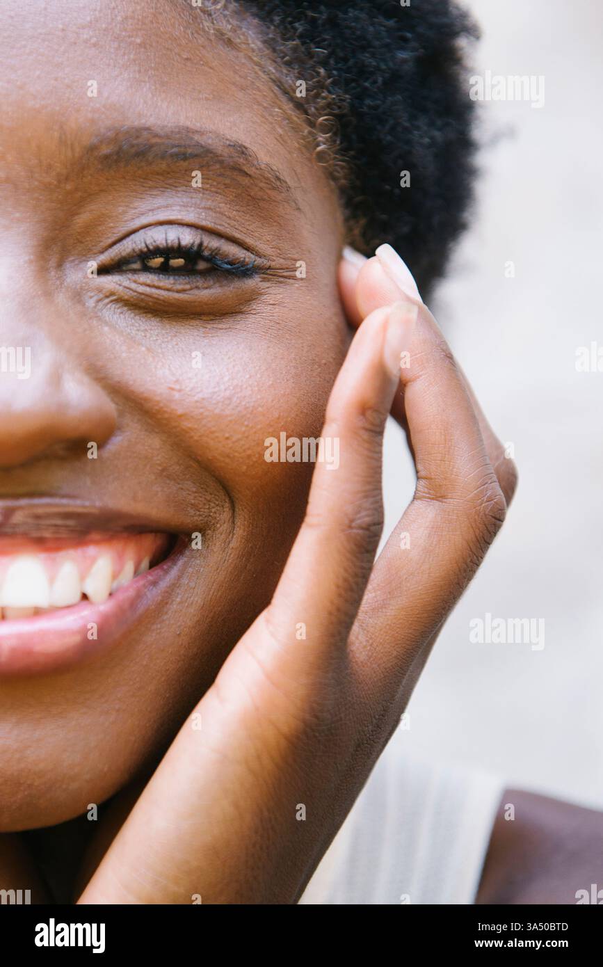 Sourire femme noire riant en appuyant son visage sur ses mains contre un mur. Un portrait lumineux qui communique bonheur, confiance et énergie positive. Banque D'Images