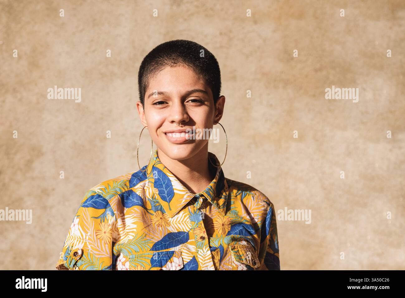 Femme hispanique souriante debout contre le mur beige à l'extérieur le jour ensoleillé Banque D'Images