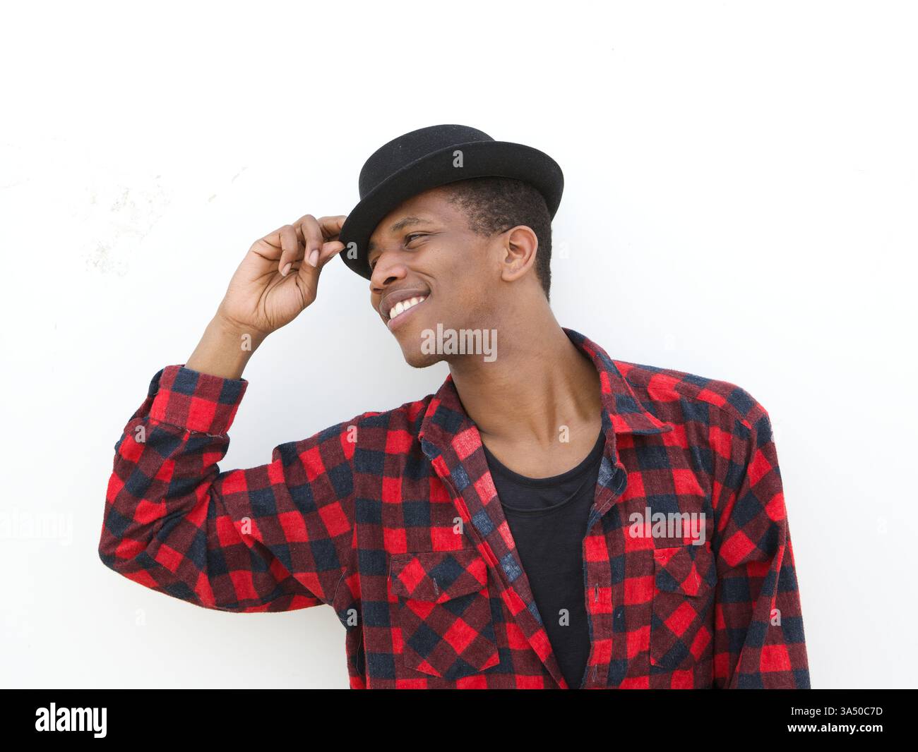 Gros plan portrait d'un jeune homme heureux souriant avec un chapeau sur un fond blanc. L'image transmet confiance et style contemporain. Convient pour la mode, le style de vie et les campagnes de marque personnelle. Banque D'Images