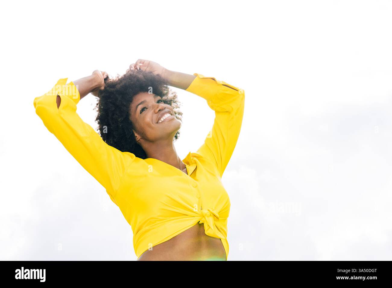 Une femme afro-américaine sourit les bras levés dans un parc ensoleillé. L'image transmet l'énergie positive, le style de vie en plein air et les vibrations estivales insouciantes. Parfait pour le bien-être, le style de vie et les messages inspirants sur la confiance et le bonheur. Banque D'Images