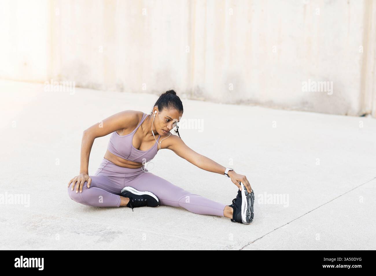 Femme afro-américaine en tenue athlétique effectuant un virage en avant sur le trottoir. La scène d'entraînement en plein air communique la forme physique, la santé et la motivation. Idéal pour les campagnes de bien-être et les images de style de vie actif. Banque D'Images