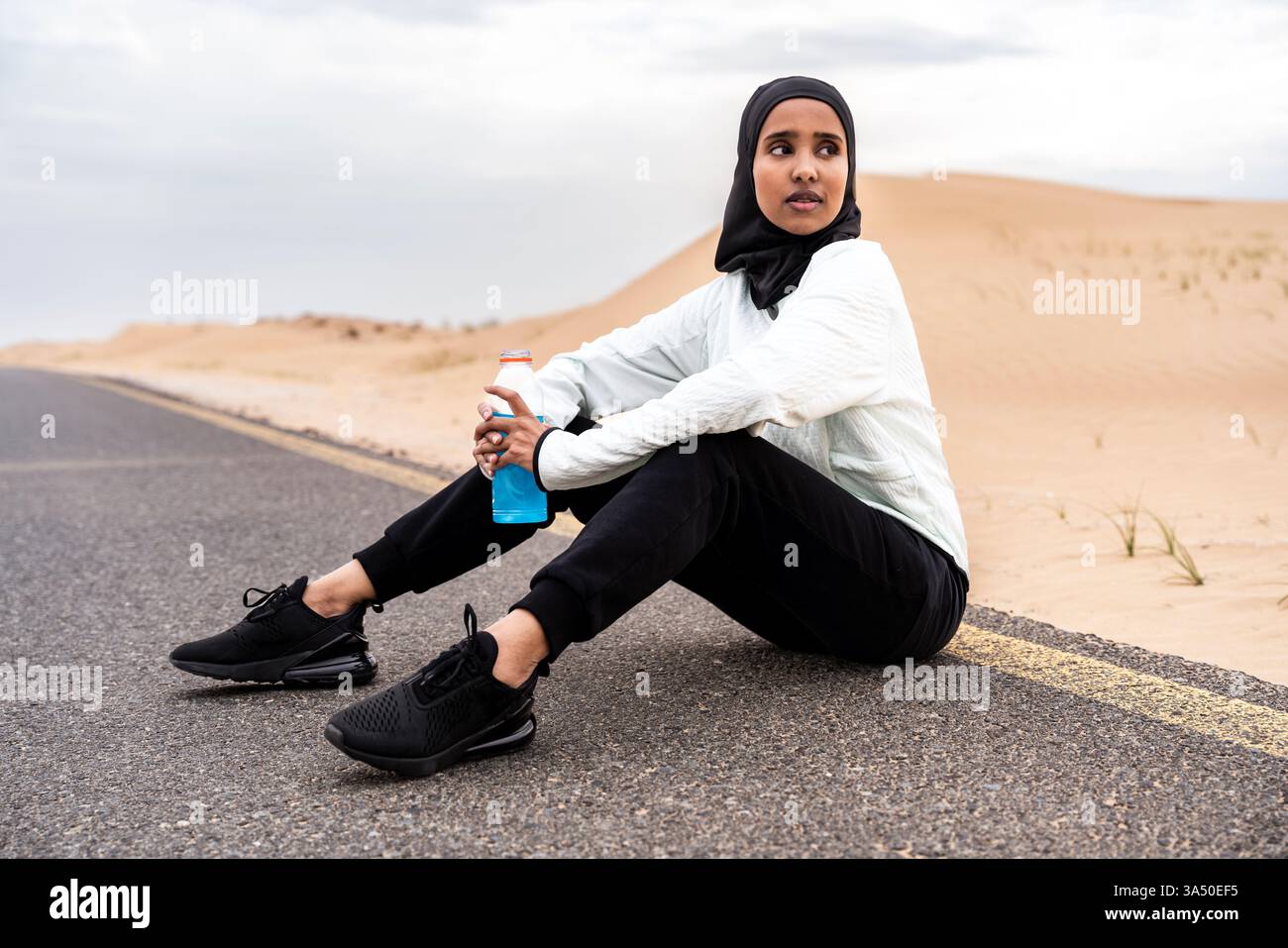 Femme musulmane active portant le hijab s'entraîne à l'extérieur dans un cadre désertique. Elle porte des vêtements de sport adaptés à la course à pied et à l'entraînement physique, y compris des vêtements de sport de style burkini. Idéal pour les campagnes sur les athlètes musulmans, l'exercice en plein air et le bien-être du désert. Banque D'Images