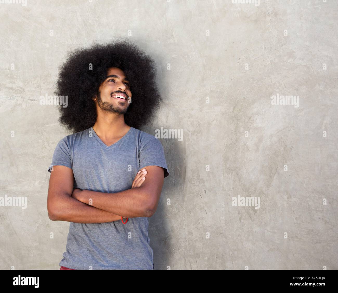 Portrait d'un homme heureux debout avec les bras croisés à côté d'un mur de béton. Ambiance moderne et confiante avec espace de copie clair pour la marque ou le texte. Convient pour les campagnes de marque personnelle, de mode et de style de vie. Banque D'Images