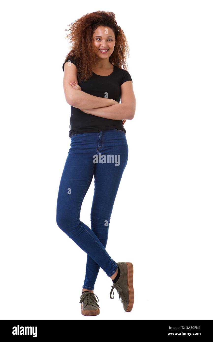 Femme afro-américaine souriante avec les cheveux bouclés se tient avec les bras croisés sur un fond blanc. Sa pose confiante et décontractée convient parfaitement aux visuels modernes et au milieu de travail. Idéal pour l'image de marque personnelle, les campagnes d'autonomisation et les communications d'entreprise. Banque D'Images