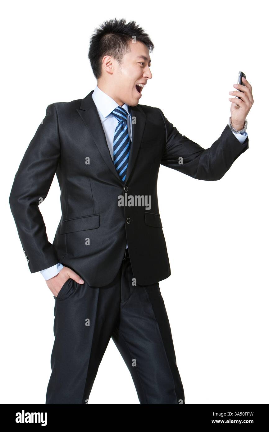 Homme d'affaires chinois dans la vingtaine, excité tout en tenant un téléphone portable. Figurine professionnelle en col blanc capturée dans une vue de trois quarts avec espace de copie pour le texte, idéale pour les thèmes commerciaux et technologiques. Idéal pour mettre en valeur la communication mobile et les moments positifs sur le lieu de travail. Banque D'Images