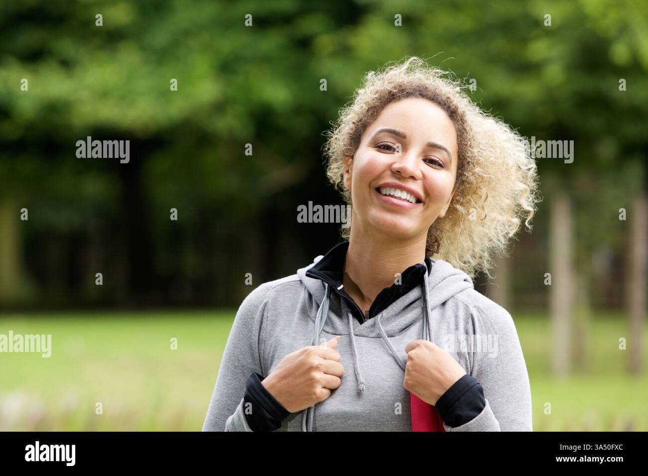Portrait extérieur d'une jeune femme noire souriante en tenue sportive, rayonnant d'énergie et de confiance. Idéal pour les campagnes de fitness, de sport et de style de vie mettant en vedette des femmes actives. L'espace de copie et la toile de fond naturelle à l'extérieur le rendent polyvalent pour la marque. Banque D'Images