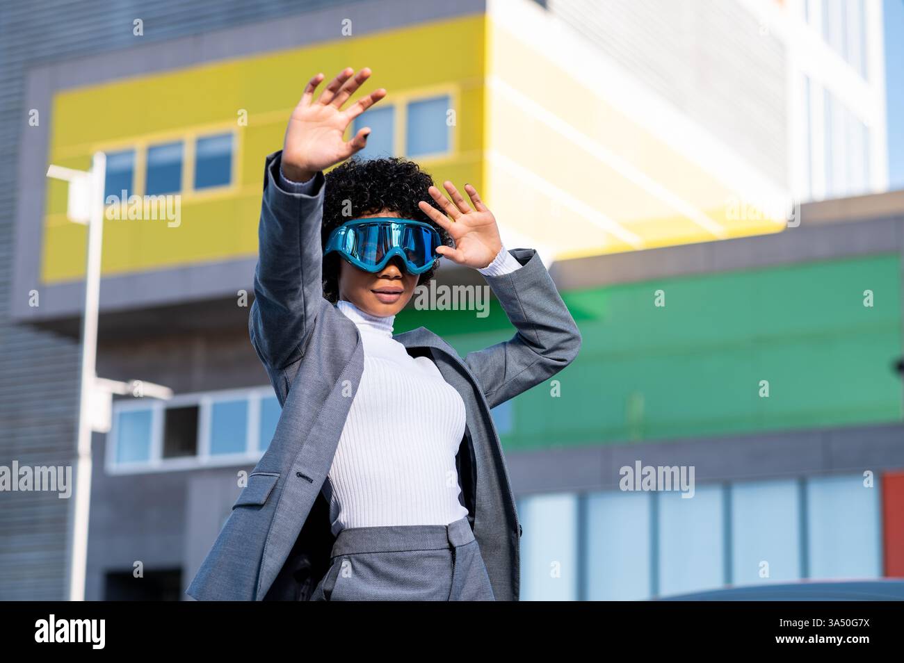Une jeune femme afro-américaine élégante portant des lunettes de ski se tient à l'extérieur dans un quartier résidentiel. Sa pose confiante et son look avant-gardiste s'adaptent au style de vie, à la vie urbaine et aux contextes de voyage. Idéal pour la mode, le style de vie et les thèmes d'activités de plein air. Banque D'Images