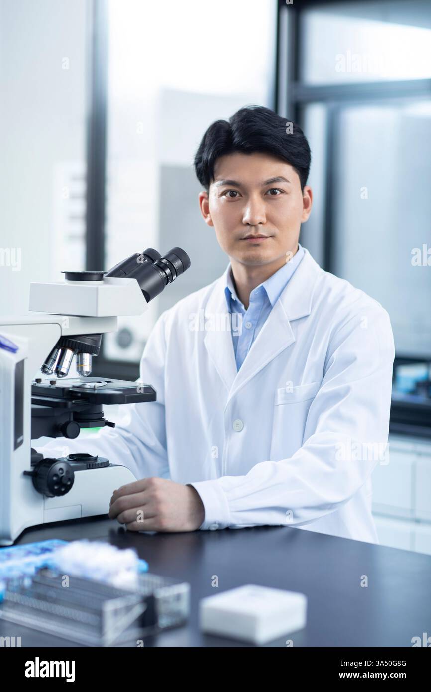 Scientifique chinois assis à table avec microscope en laboratoire Banque D'Images