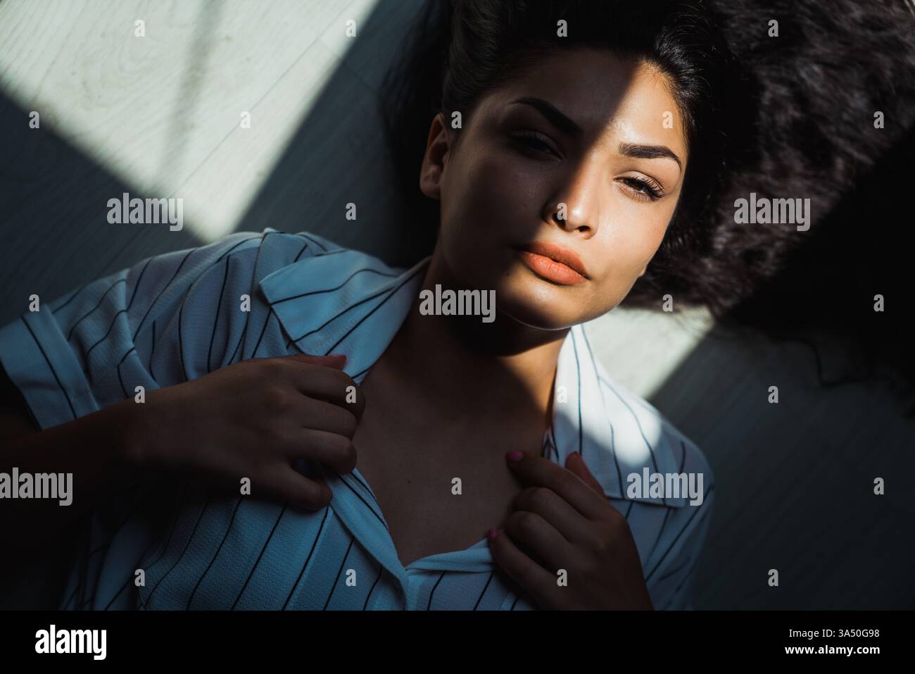 Femme hispanique sérieuse allongée sur un sol ensoleillé à la maison avec les mains sur son col. Une image de style de vie contemplative adaptée à la vie à la maison, à la détente et aux moments personnels. Banque D'Images