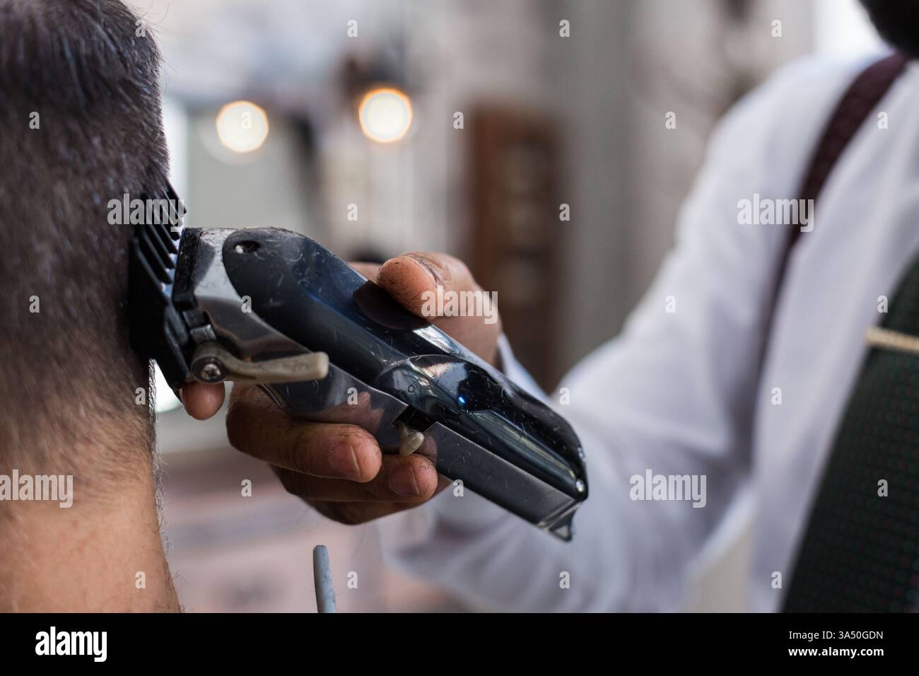Coiffeur hispanique taillant les cheveux de l'homme caucasien à l'aide de la tondeuse dans le salon de coiffure Banque D'Images