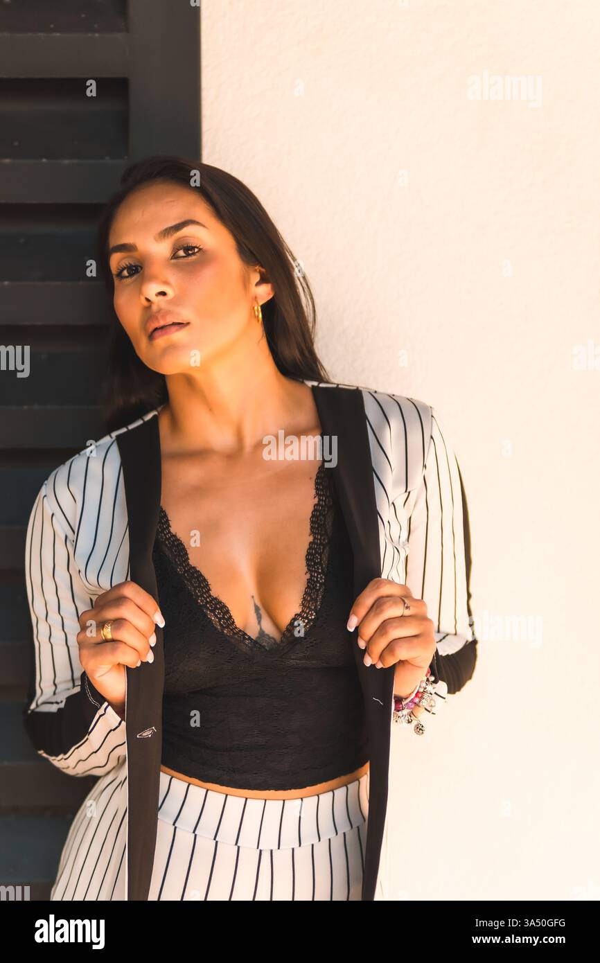 Portrait de style de vie d'une femme latine élégante dans un costume blanc avec des rayures noires, posé sur un fond noir et blanc fendu. Le look avant-gardiste transmet l'élégance chic et la confiance. Idéal pour la mode, les portefeuilles de modèles et les campagnes Street style. Banque D'Images