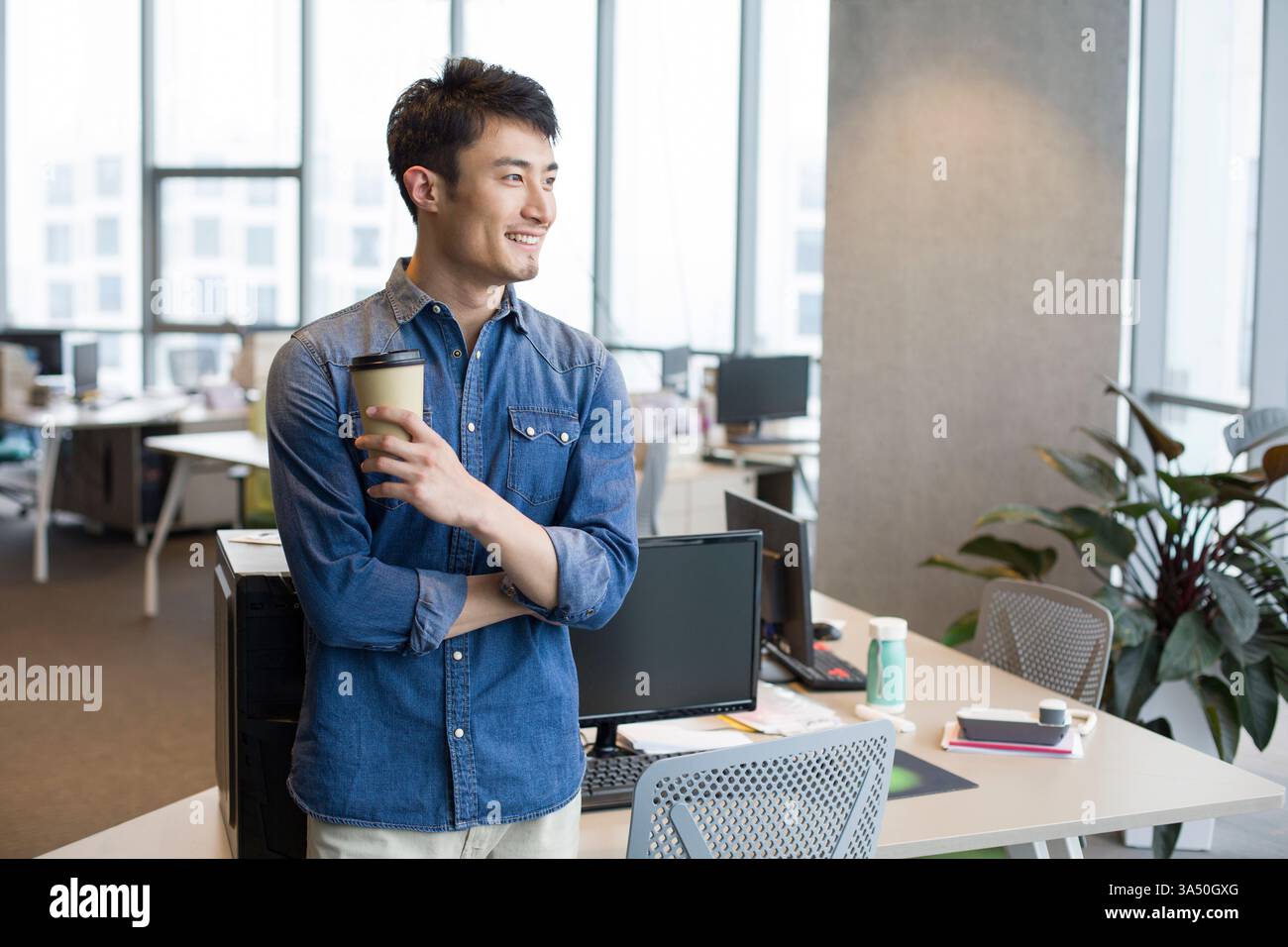 Jeune Chinois prenant une pause café dans un bureau. Une scène détendue et contemporaine adaptée aux affaires, au lieu de travail et aux campagnes de style de vie urbain. Banque D'Images