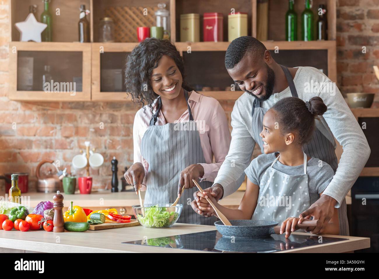 Joyeuse famille noire portant des tabliers debout au comptoir de cuisine cuisiner ensemble à la maison Banque D'Images