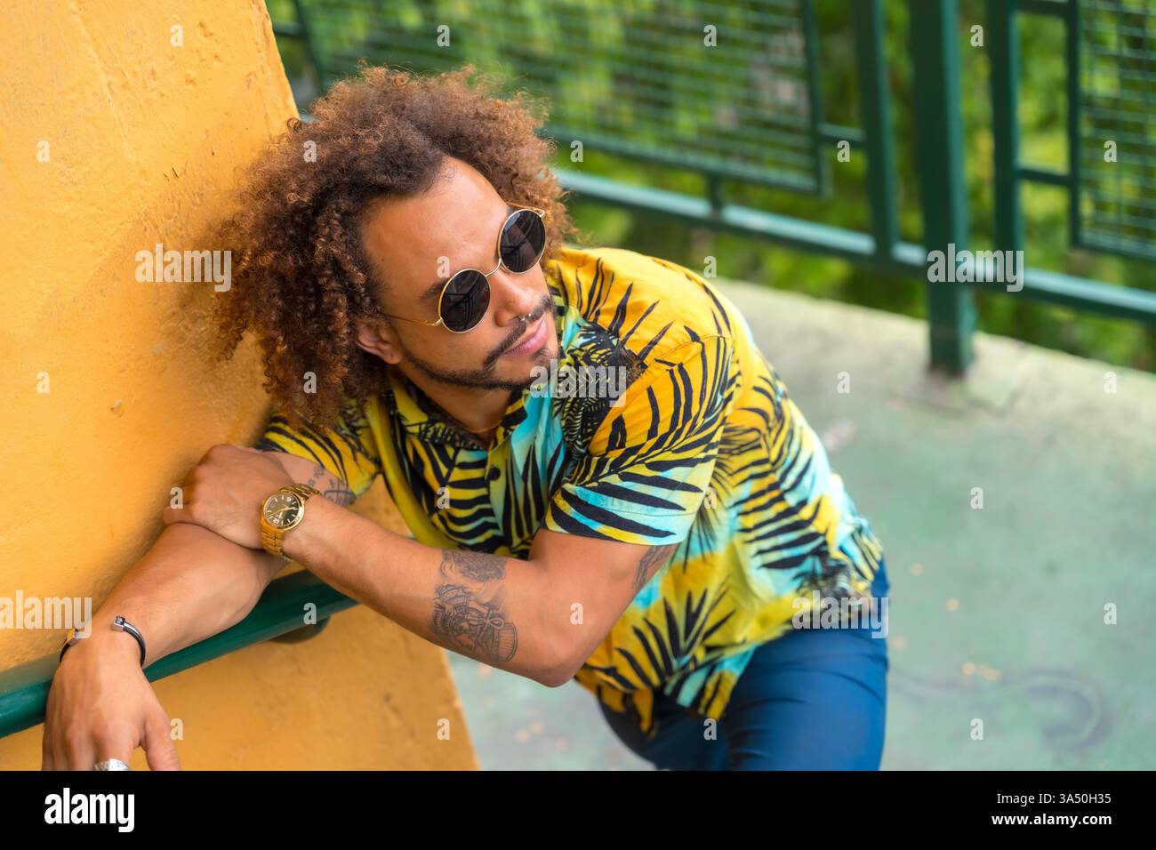 Homme hispanique avec des cheveux afro portant une chemise imprimée palmier sur un fond jaune vif, exsudant le style de l'été. Parfait pour la mode, le style de vie et les campagnes estivales. Banque D'Images