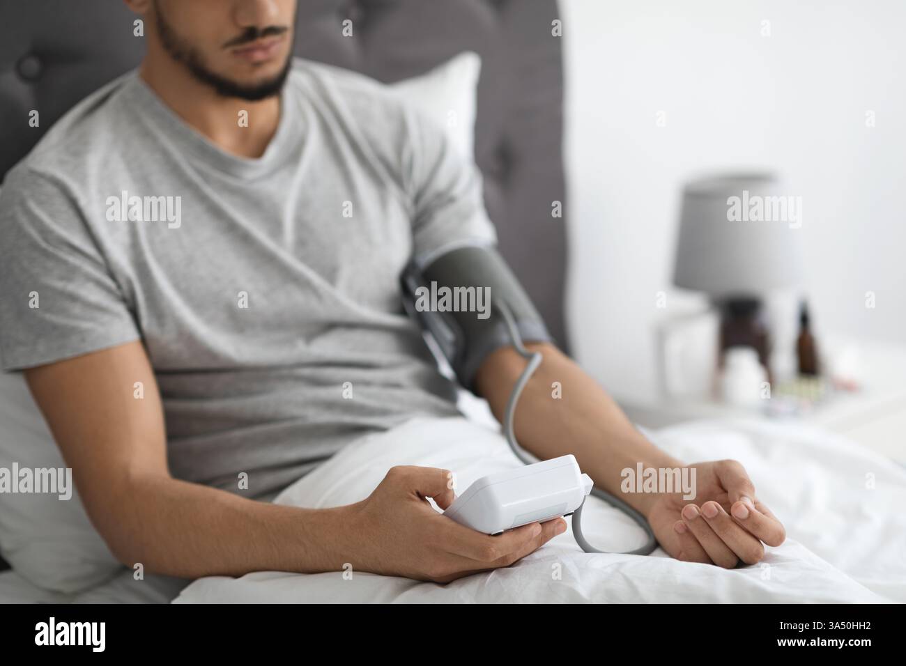 Homme arabe assis dans le lit et vérifiant la pression artérielle avec le moniteur du bras supérieur, gars méconnaissable du moyen-Orient mesurant la tension artérielle au repos Banque D'Images