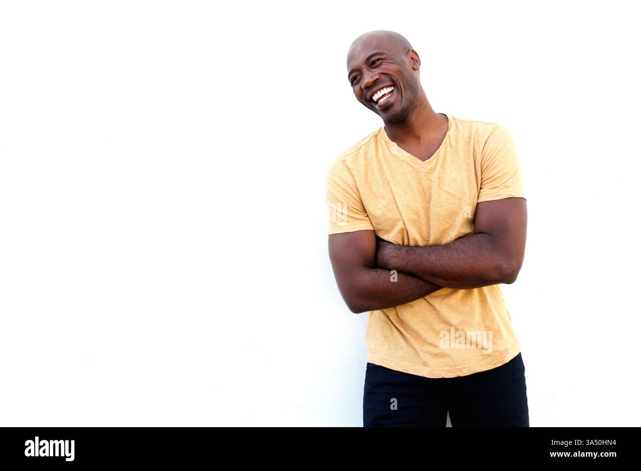 Joyeux homme noir se tient avec les bras croisés sur un fond blanc propre. Le portrait offre un espace de copie clair pour les titres et le texte, transmettant confiance et style contemporain. Idéal pour les campagnes sur la réussite professionnelle, l'image de marque personnelle ou la mode. Banque D'Images