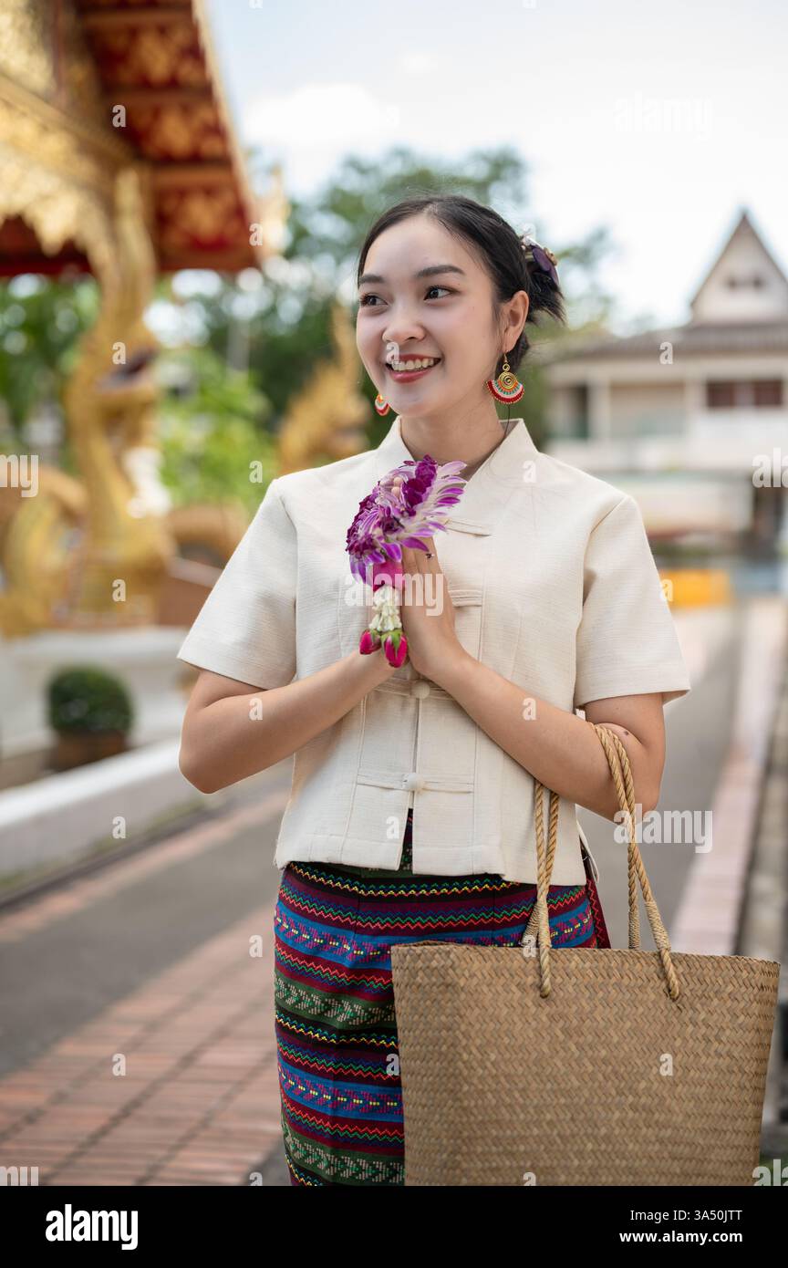 Une belle femme thaïlandaise en robe traditionnelle nordique se tient dans un temple dans une pose de prière, tenant une guirlande. Situé dans un temple de Chiang mai, l'image transmet la culture, la spiritualité et le respect. Idéal pour les voyages culturels, le patrimoine bouddhiste et l'imagerie de l'Asie du Sud-est. Banque D'Images