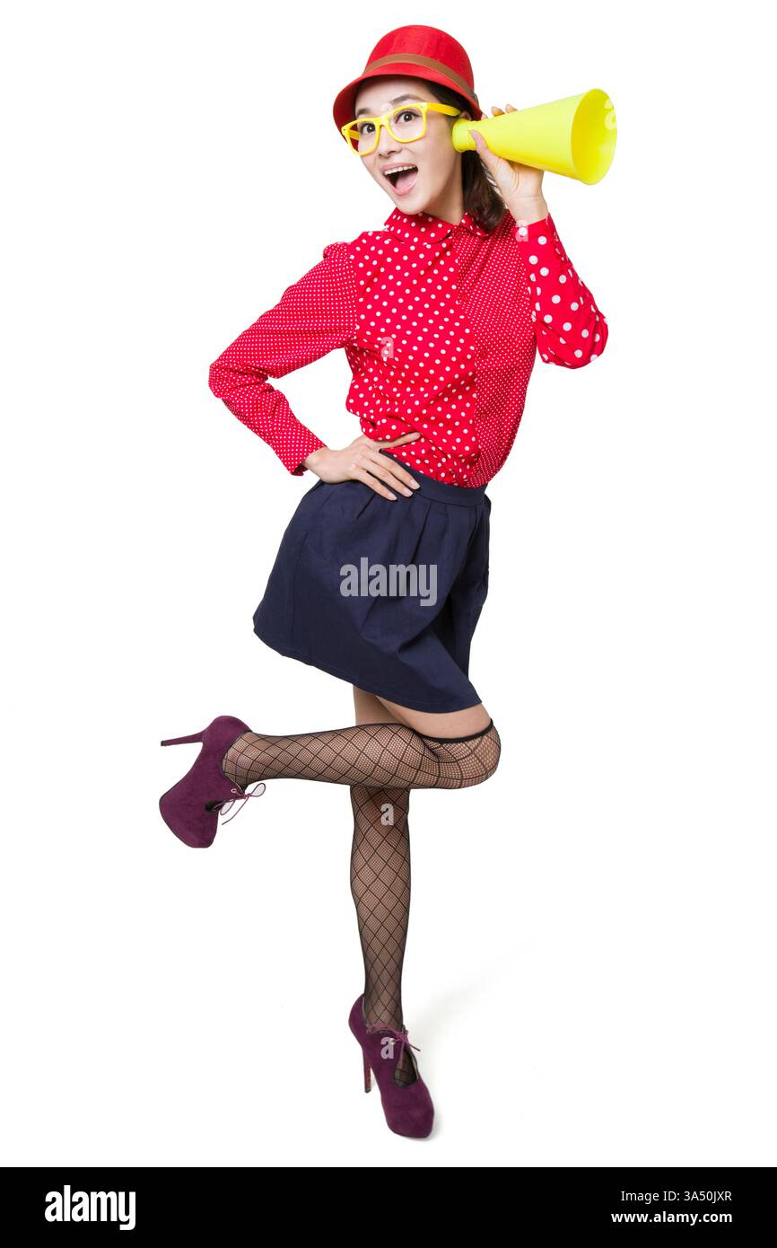 Jeune femme chinoise écoutant à travers un mégaphone, exsudant excitation et énergie positive. L’image suggère des annonces, de la curiosité et des découvertes ludiques. Convient pour les campagnes sur les événements, la culture de la jeunesse et les nouvelles dans un contexte moderne. Banque D'Images
