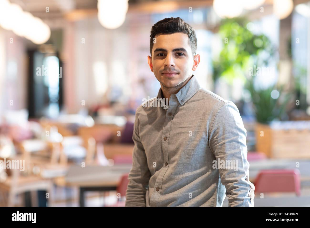 Debout dans un café confortable, cet homme du moyen-Orient respire la confiance décontractée. Le cadre intérieur crée un moment de style de vie naturel adapté à la culture du café, la vie étudiante ou le contenu du travail urbain. Banque D'Images