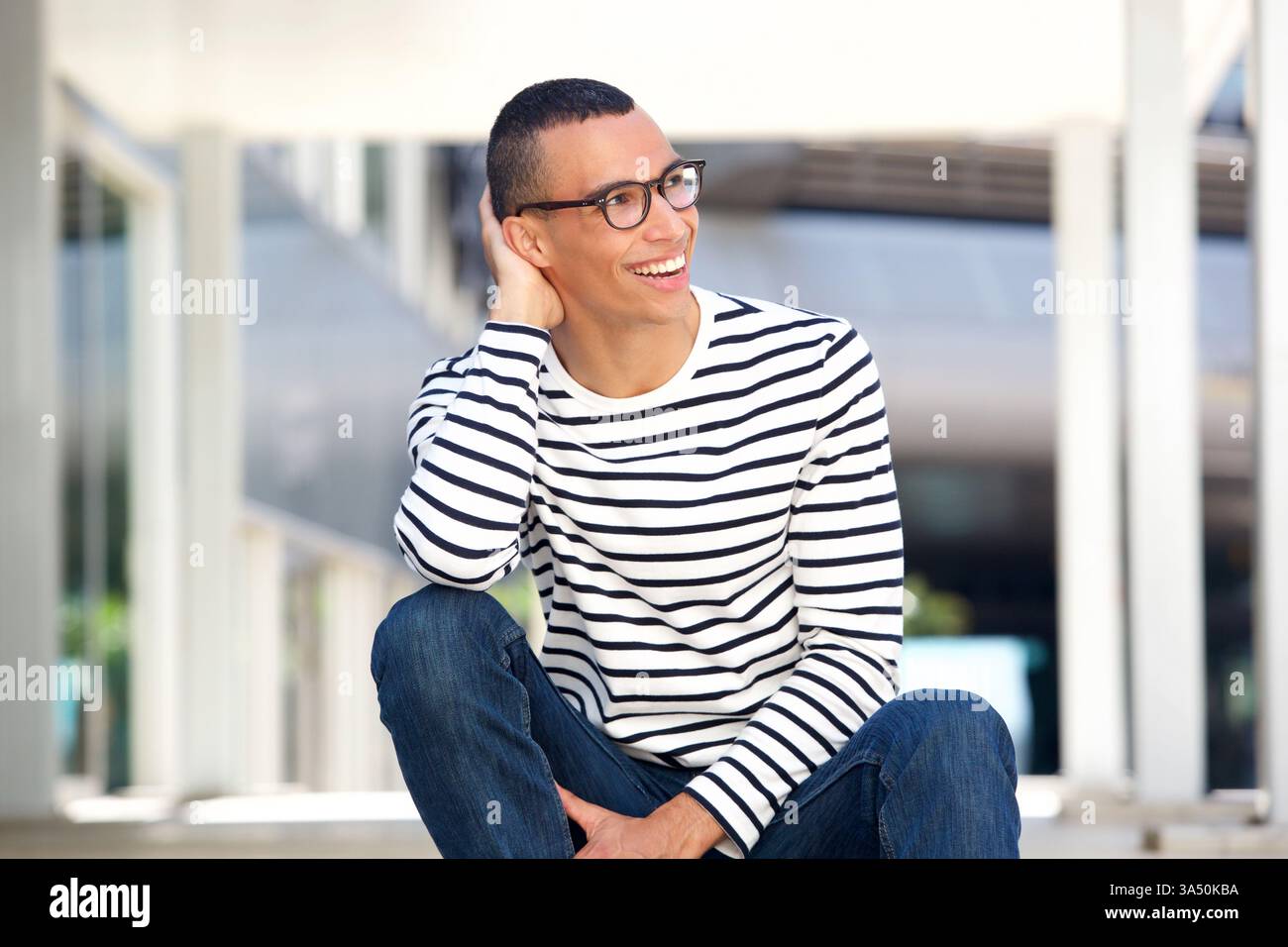 Portrait d'un beau jeune homme portant des lunettes, assis dehors. Une image de style de vie et de mode polyvalente pour l'image de marque personnelle, le travail moderne ou les profils professionnels. Le look accessible fonctionne pour la technologie, l'éducation et les industries créatives. Banque D'Images