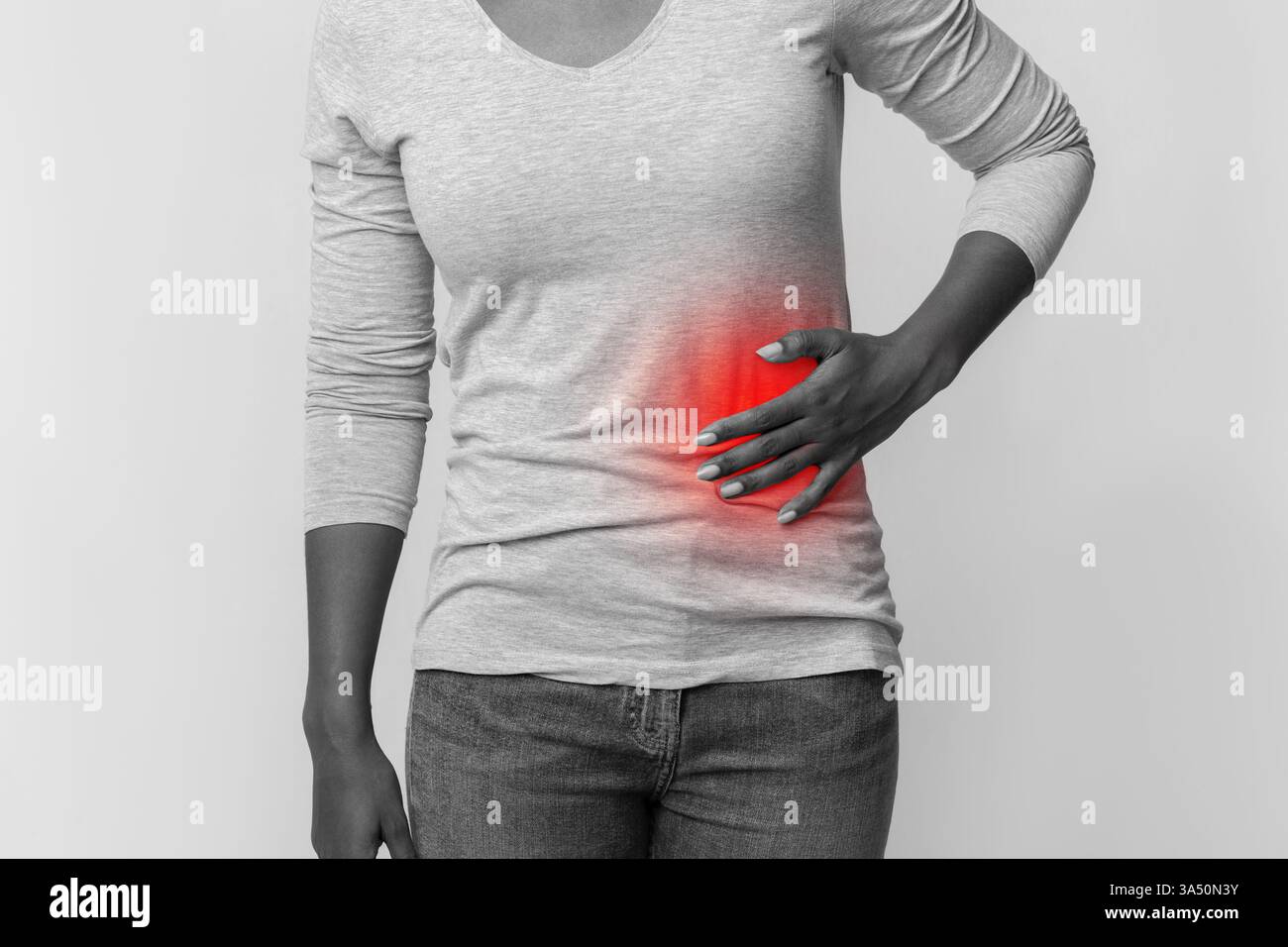 Portrait recadré noir et blanc d'une femme africaine tenant son abdomen gauche, véhiculant des concepts de pancréatite. Le tournage en studio met l'accent sur la douleur abdominale et la maladie pour les messages de soins de santé. Adapté aux articles médicaux, à l'éducation des patients et aux campagnes de sensibilisation aux maladies. Banque D'Images