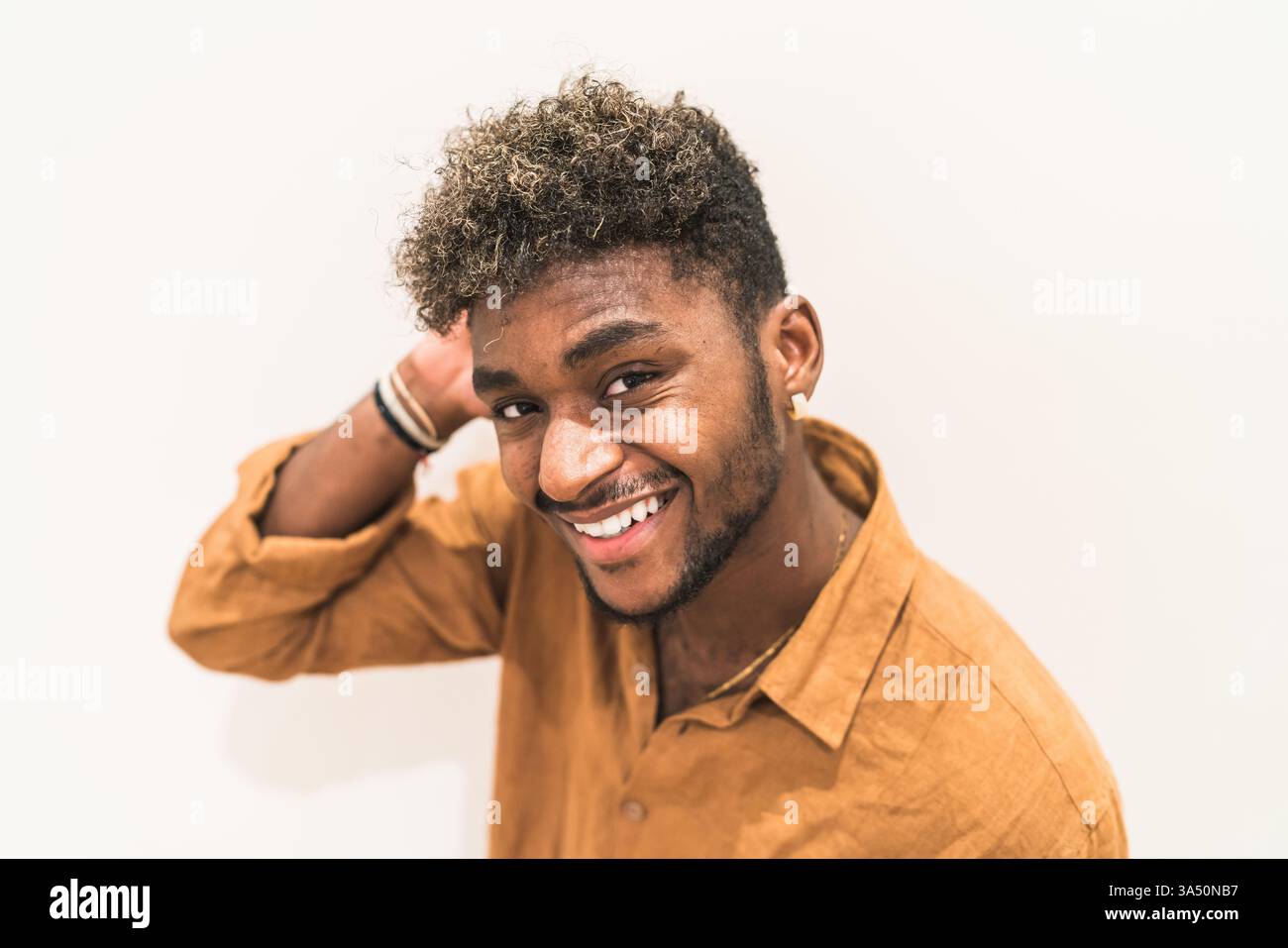 Portrait d'un homme noir souriant avec des cheveux bouclés debout sur un fond blanc. Le style décontracté et contemporain le rend adapté à l'utilisation de style de vie, d'entreprise ou de marque personnelle. Positive et accessible, elle communique confiance et chaleur. Banque D'Images