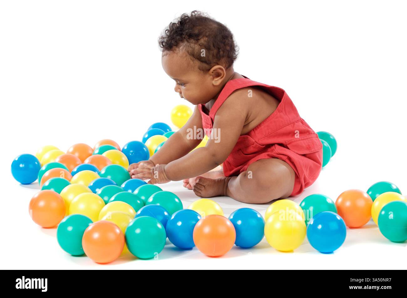 Bébé fille noire jouant avec des boules en plastique colorées tout en étant assis sur fond blanc Banque D'Images