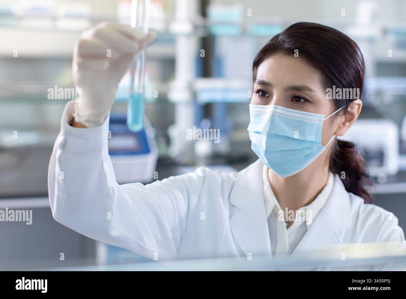 Scientifique chinois examinant un échantillon médical dans un laboratoire. Adapté à la biotechnologie, à la recherche médicale et à l'imagerie médicale. Vue de face d'une scientifique féminine concentrée dans un laboratoire professionnel. Banque D'Images