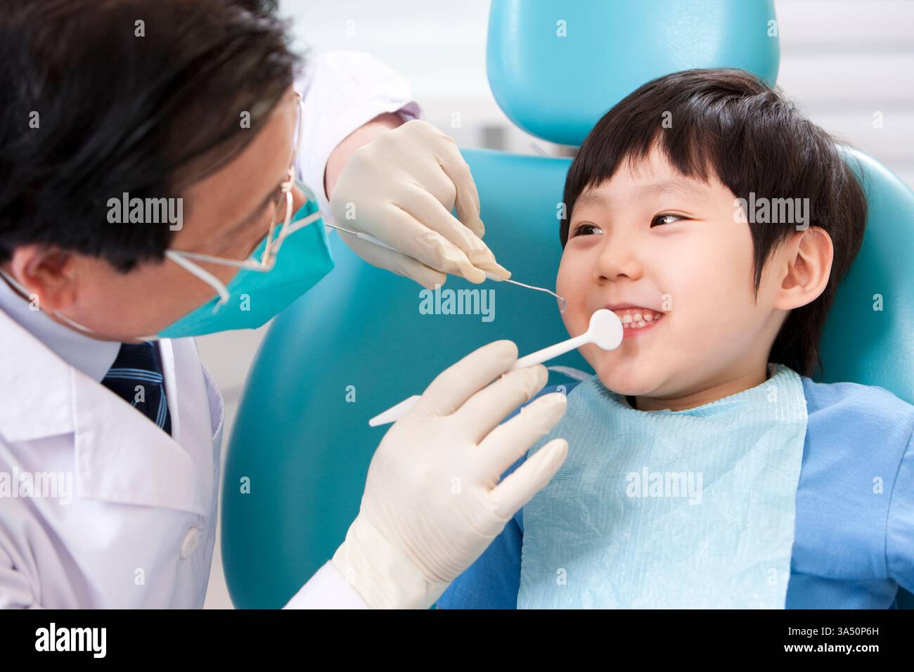 Garçon chinois souriant recevant un traitement d'un dentiste masculin senior assis dans une chaise dentaire. La scène transmet la confiance, la santé dentaire et les soins professionnels dans une clinique. Banque D'Images