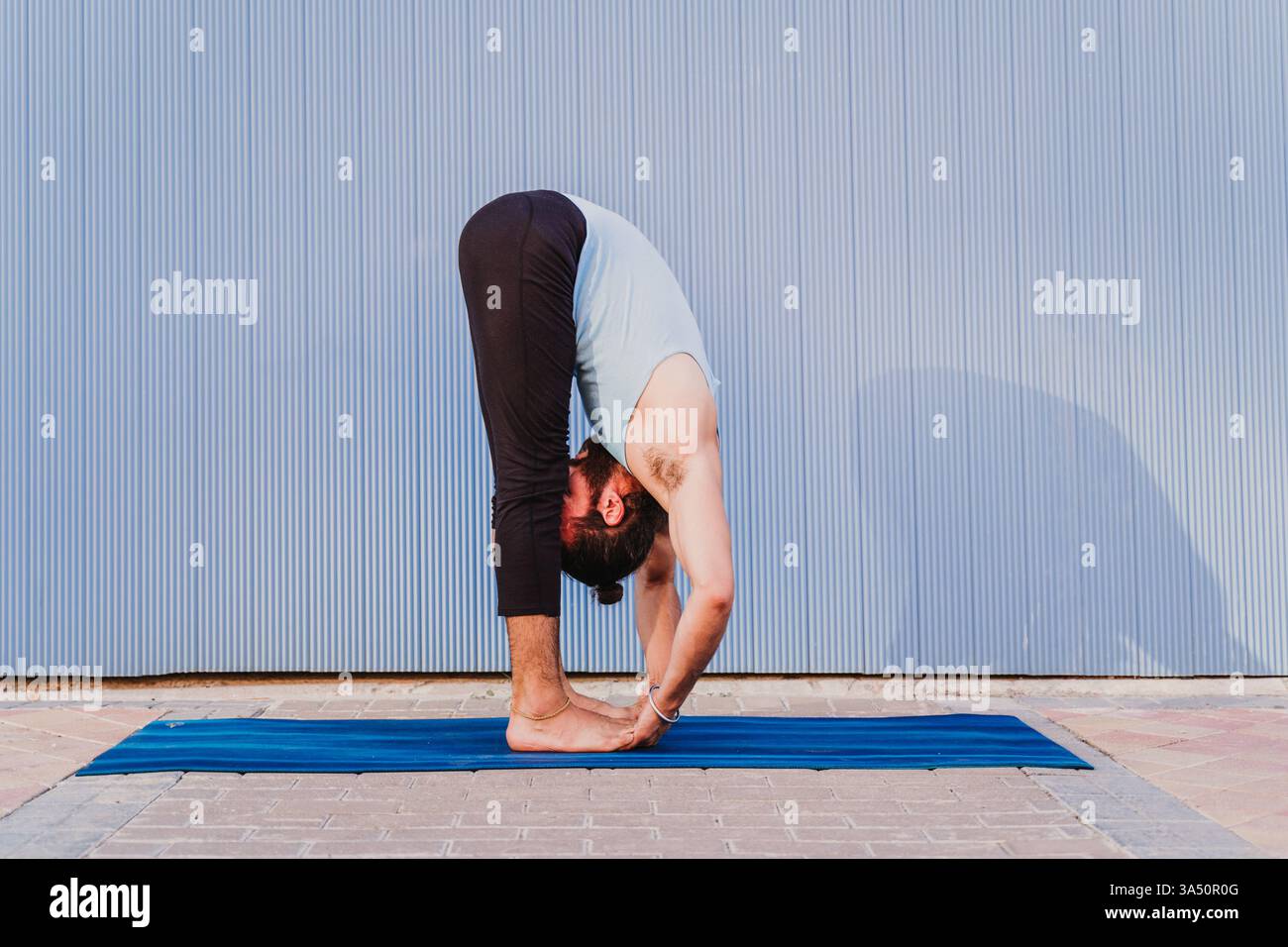 Portrait de yoga urbain d'un homme en tenue sportive pratiquant le yoga sur fond bleu. Met l'accent sur la santé, le bien-être et un mode de vie actif dans les environs de la ville. Banque D'Images