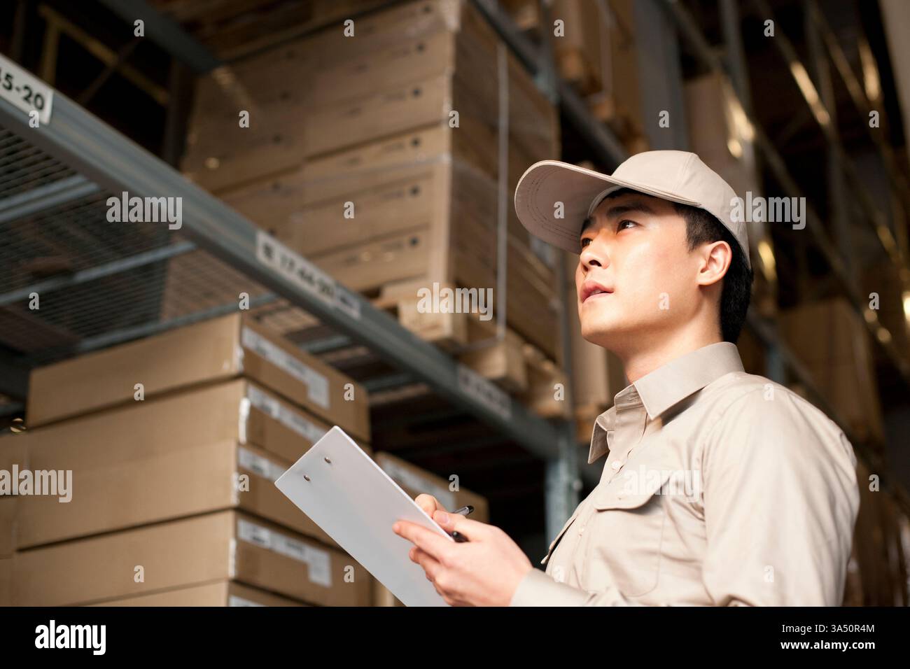 Ouvrier masculin chinois d'entrepôt avec presse-papiers dans un environnement logistique. Adapté aux thèmes de la chaîne d'approvisionnement, de l'entreposage et des opérations. Banque D'Images