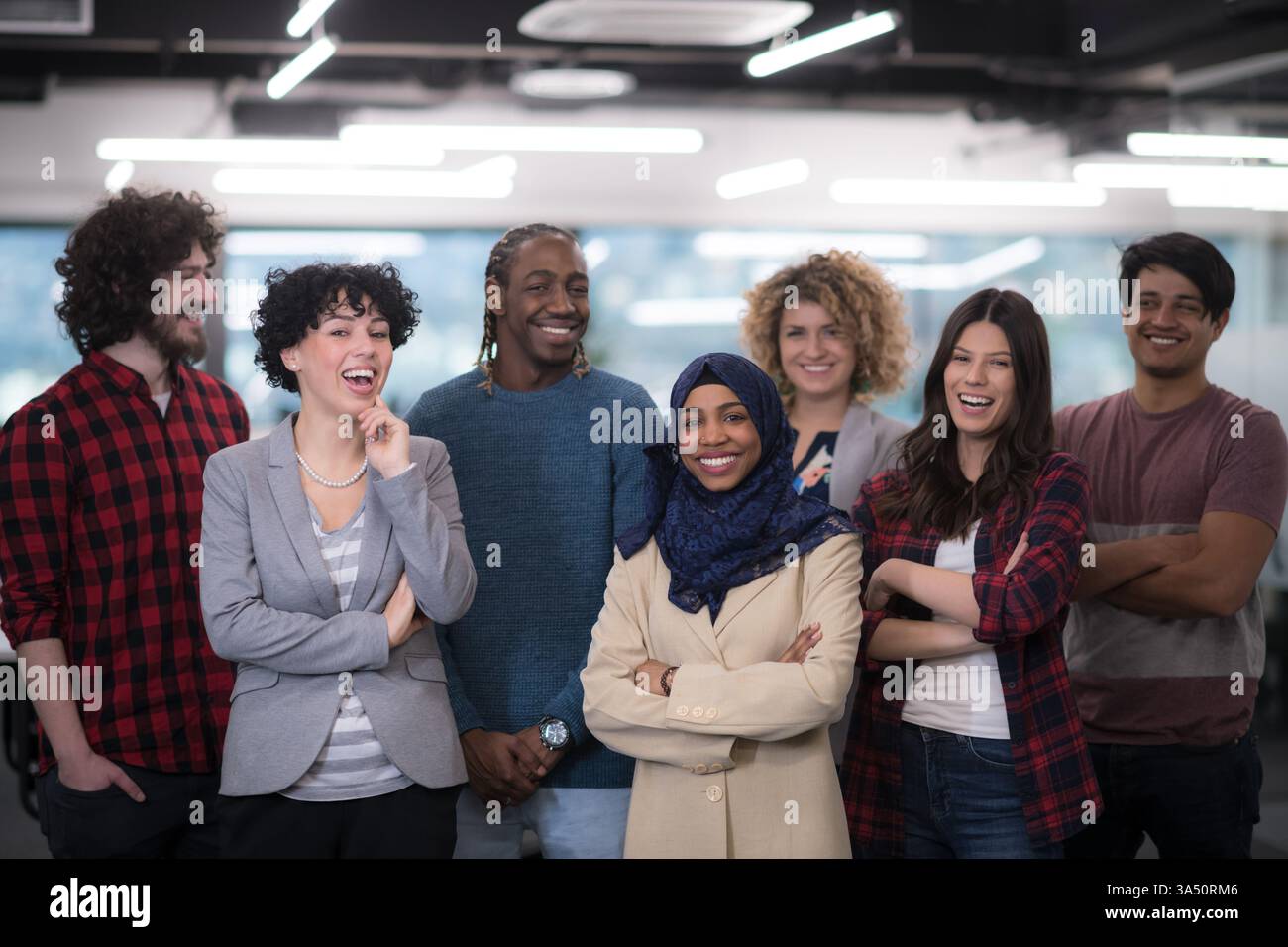 Portrait d'une équipe de développement de logiciels diversifiée célébrant le succès dans une startup moderne. Le groupe enthousiaste se tourne vers la caméra, véhiculant le travail d'équipe, l'innovation et l'énergie entrepreneuriale dans un bureau contemporain. Banque D'Images