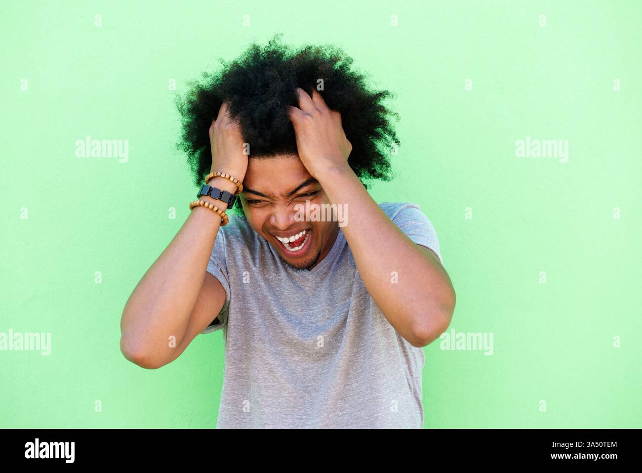 Portrait en gros plan d'un jeune homme noir émotionnel avec les mains dans les cheveux. Une image expressive pour des sujets sur le stress, l'anxiété, l'humeur et la santé mentale, ainsi que les caractéristiques du style de vie contemporain. Adapté aux campagnes sur le bien-être et la résilience personnelle. Banque D'Images