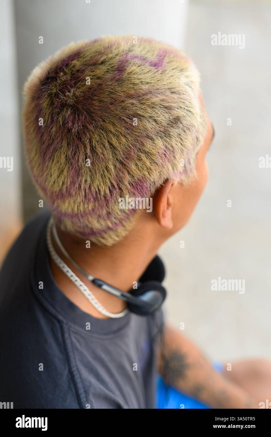 Vue arrière d'un homme avec les cheveux teints et un tatouage à la main debout dans un cadre lumineux à la maison. Le portrait de style de vie contemporain met l'accent sur l'individualité et le style personnel. Pratique pour les fonctionnalités sur la mode, l'expression de soi et la vie moderne. Banque D'Images